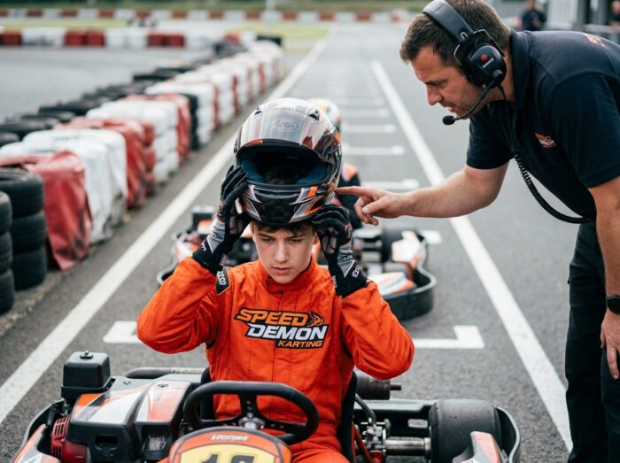 Jeune pilote de karting enfilant son casque sous les conseils d'un instructeur sur la grille de départ